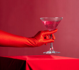 Female hand in red glove hold red cocktail on red background