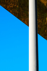 A simple pole stands beneath a bright blue sky and sharp angular canopy, creating a minimalist...