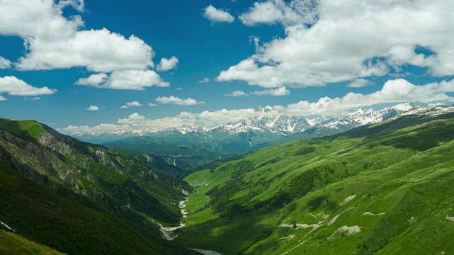 Timelapse of Ushba peak in Svaneti Greater Caucasus Mountain Range. Green valley, snow-capped peaks, rolling clouds. Scenic natural landscape, changing weather over time. Seasonal transitions.