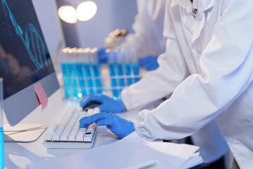 Close-up of a scientist wearing blue gloves typing on a keyboard, with a dna double helix displayed on the computer screen in a modern laboratory setting, suggesting genetic research and analysis