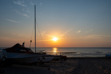 Sunset over the sea, with sandy beach and sailboats on land
