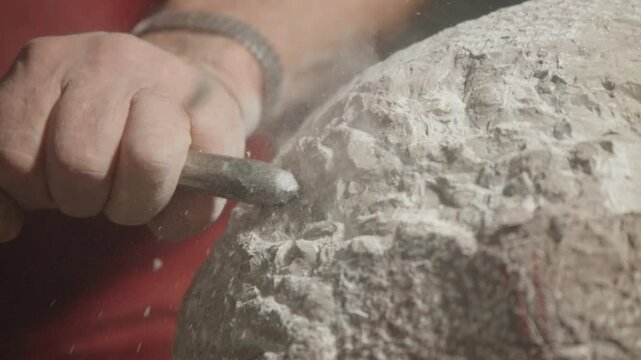 Close-up view about the moment of artistic stone carving with a man and his hammer tool, Italy.