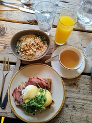 A wooden breakfast table with orange juice, herbal tea, a granola bowl, and eggs Benedict, emphasizing health, nutrition, and good taste.