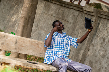 African American man seated in the garden calmly using phone for leisure, Technology, game, gamer, gaming, connection