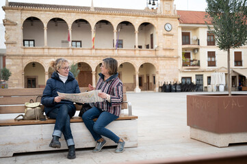 Two senior women reviewing a map while exploring a historic Spanish plaza on a cultural sightseeing...