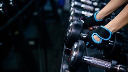 Close-up of woman wearing gym gloves lifting dumbbells in a gym