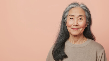 Portrait of a beautiful smiling senior asian woman with long gray hair posing on a pink background, showing confidence and serenity