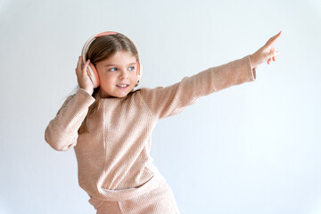 Portrait of a girl 8 years old in mocha headphones, listening to music and showing a hand gesture. Free time.