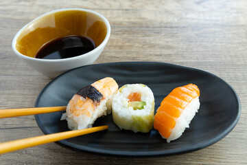 a black design plate with sushi and chopsticks and soybean vol on a wooden table of an elegant restaurant. photo from above top