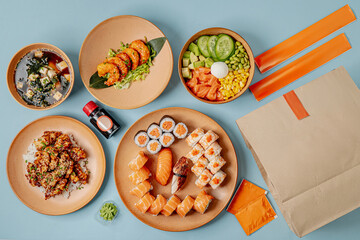 Japanese cuisine assortment with sushi, poke bowl, miso soup, and teriyaki chicken arranged on a blue background.