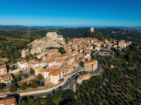 Aerial view of picturesque medieval town with stone structures and olive trees nestled in hills, Castiglione d'Orcia, Italy.