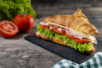 Croissant with ham, cheese and vegetables on wooden table