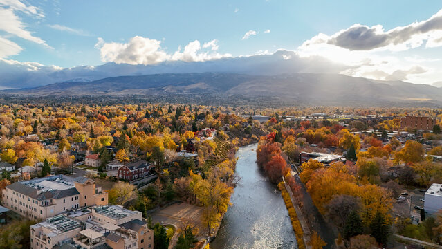 Aerial view of vibrant autumn foliage and serene river with picturesque mountains and cityscape, Downtown Reno, United States.