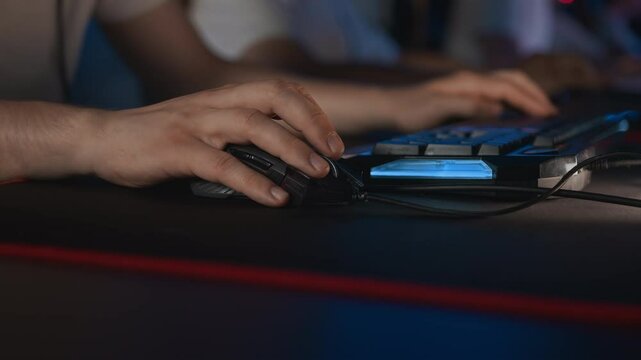 Gamer plays video game on PC at computer club with his team, professional cyber sport tournament, gaming mouse RGB lighting keyboard on mat close up. E-sport championship. Multiplayer shooter strategy