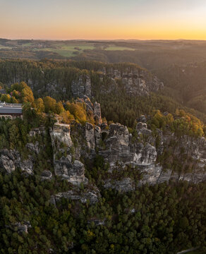 Aerial view of Basteibrucke bridge over the Elbe river with surrounding rocks and trees at sunrise, Basteibrucke, Germany.