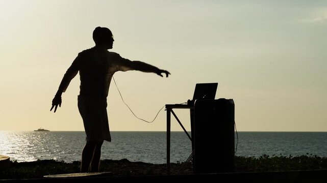 DJ playing music on the beach by the sea at sunset