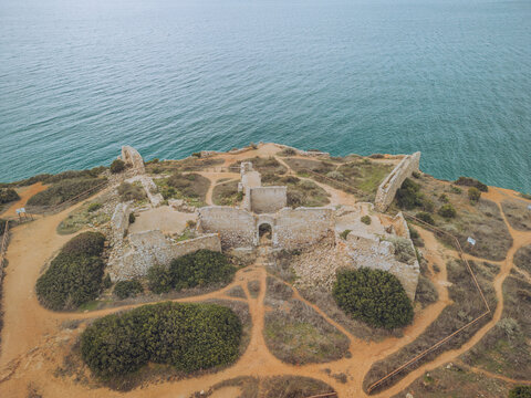 Aerial view of ancient ruins of Forte de Almadena on a rocky cliff by the sea, Budens, Portugal.