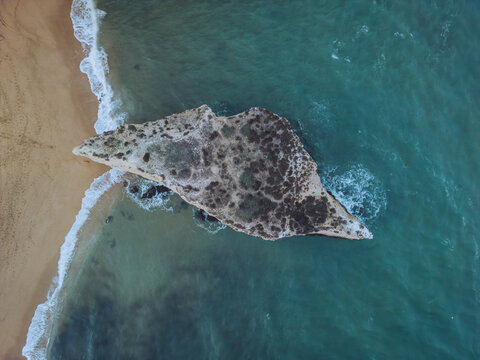 Aerial view of praia da cova redonda with a beautiful sea stack and tranquil ocean, Porches, Portugal.