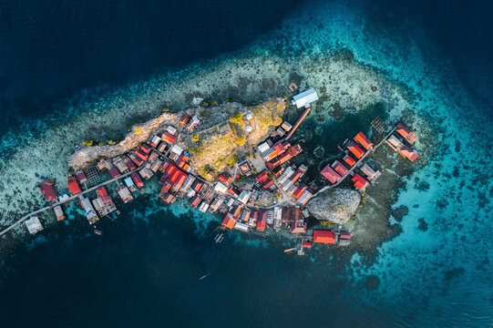 Aerial view of traditional sea houses and boardwalk in a serene coastal village, Walea Kepulauan, Indonesia.