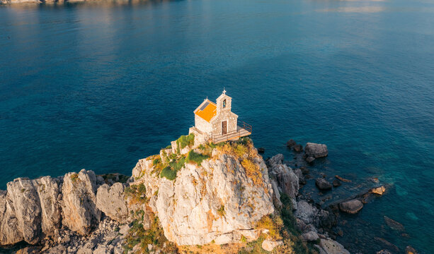 Aerial view of st. nedjelja church on a rocky island with tranquil blue sea and scenic cliffs, petrovac, montenegro.