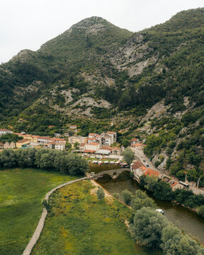 Aerial view of picturesque river town nestled among lush mountains with a scenic bridge, Rijeka Crnojevica, Montenegro.