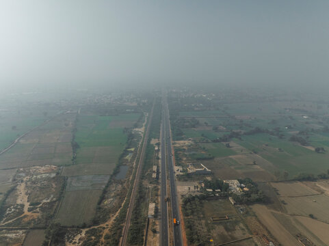 Aerial view of expansive expressway surrounded by serene fields and cloudy sky, Bharhkol, Fatehpur Sikri, Uttar Pradesh, India.