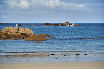 Two fishing boats anchored in the serene blue sea, surrounded by rocks and calm waters under a...