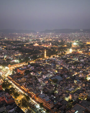 Aerial view of vibrant illuminated cityscape at twilight with bustling rooftops and historic architecture, Jaipur, India.