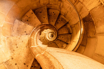 A mesmerizing spiral staircase of stone, illuminated by warm golden light, draws the viewer's eye...