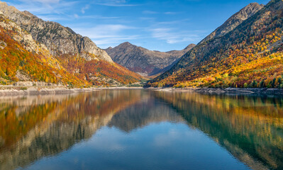 The serene Embalse de Linsoles in Posets-Maladeta Natural Park reflects vibrant autumn colors, framed by majestic Pyrenean peaks and lush alpine forests.