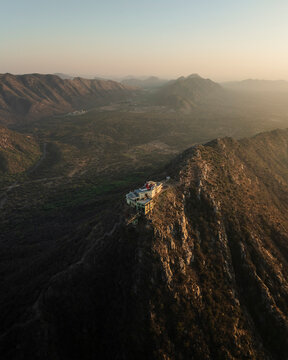 Aerial view of Shree Savitri Mata Temple on a hilltop surrounded by majestic mountains and a tranquil valley at sunset, Pushkar, Rajasthan, India.
