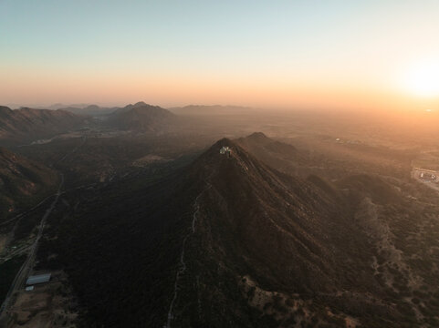Aerial view of the majestic Shree Savitri Mata Temple surrounded by serene mountains and a tranquil valley at sunrise, Pushkar, Rajasthan, India.