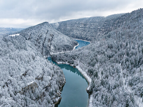 Aerial view of snowy landscape in the valley of River Doubs surrounded by majestic mountains and tranquil forests, Les Brenets, Switzerland.