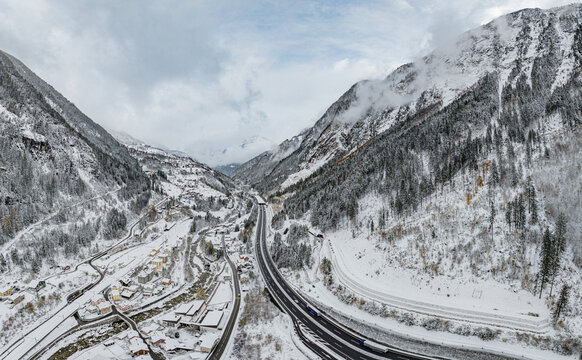 Aerial view of snowy mountains and a serene village along highway A2 in a tranquil valley, Gurtnellen, Switzerland.