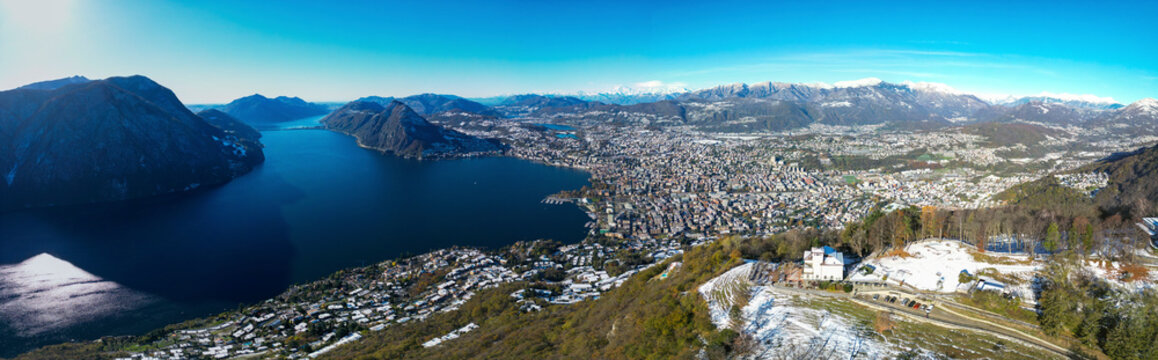 Aerial view of picturesque Lake Lugano surrounded by majestic mountains and vibrant cityscape, Bre sopra Lugano, Switzerland.