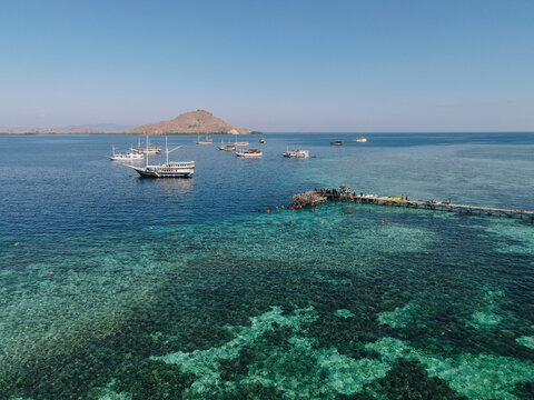 Aerial view of Kanawa Island beach with long bridge dock and sailing boats around.