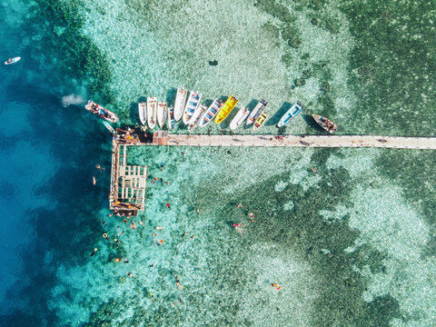 Aerial view of Kanawa Island beach with long bridge dock and sailing boats around.