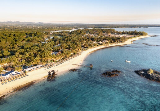 Aerial view of beautiful white sand beach and azure ocean with palm trees and sunbeds at Constance Belle Mare Plage resort, Pointe de Flacq, Mauritius.