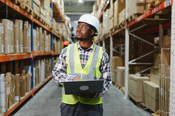 African american Warehouseman checking delivery, stock in warehouse on laptop. Warehouse manager...
