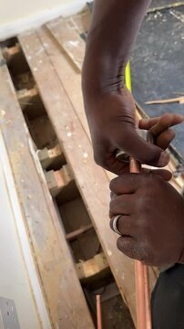 Vertical video. Black plumber cutting copper pipe using manual cutter and deburring sharp edge of tube indoors, close-up.