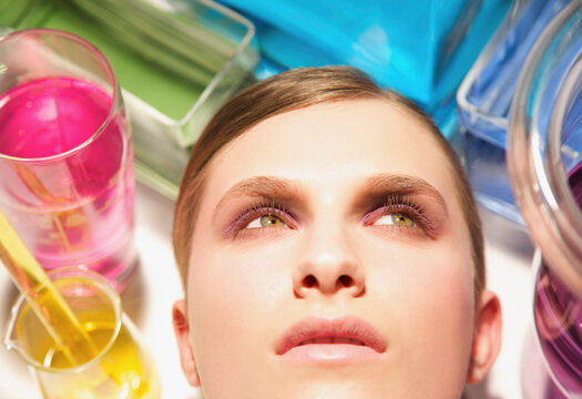 Close up of a young woman face surrounded by chemical glassware
