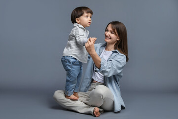 Happy mother with her little son on grey background