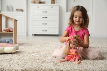 Cute little girl playing with her doll on floor at home. Space for text
