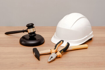 Construction law concept with judge gavel, safety helmet, hammer and pliers lying on wooden table