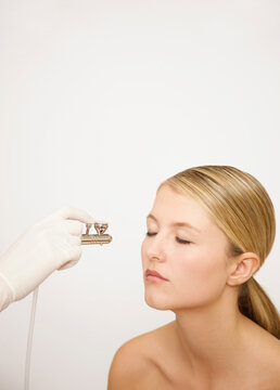Beautician's hand applying make up with an airbrush to a woman's face
