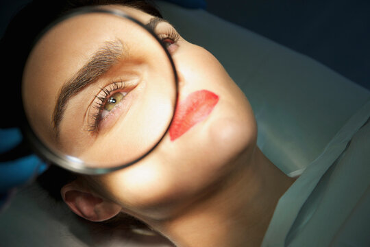 Doctor's Hand Holding Magnifying Glass over Woman's Eye
