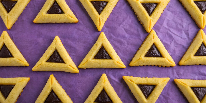 Triangular hamantaschen cookies arranged on purple background