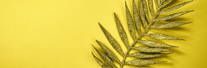 Close-up of a golden fern leaf placed on a vibrant yellow background, ideal for modern and...