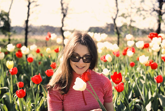 Portrait young brunette woman in sunny spring field with red and white tulips
