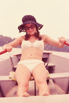 Portrait happy young woman in bikini and sun hat rowing canoe
